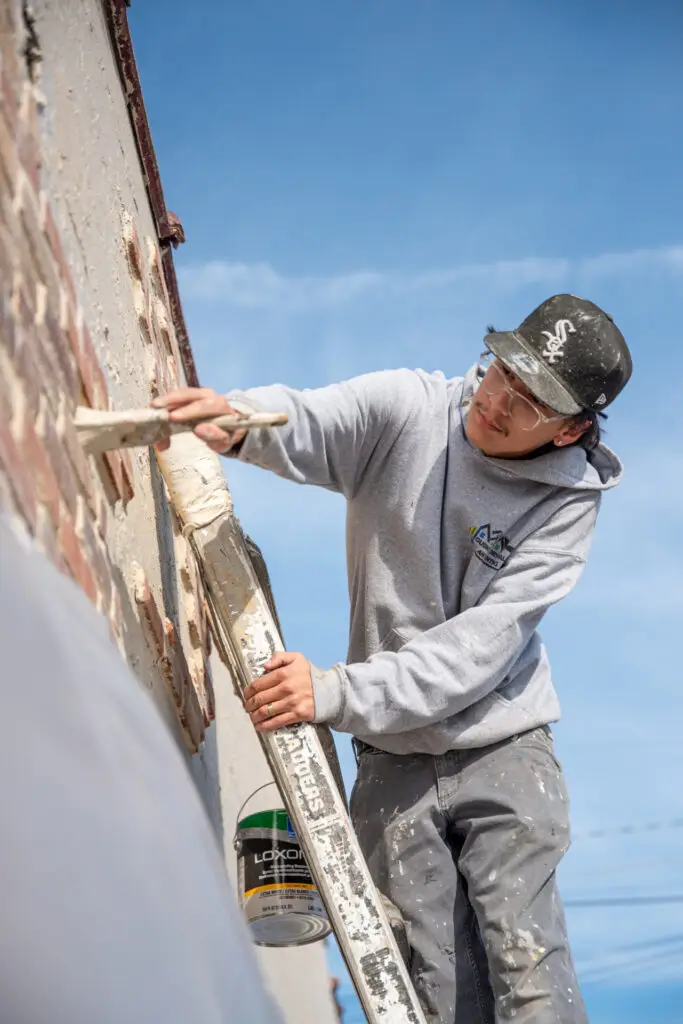 Young man painting side of brick building