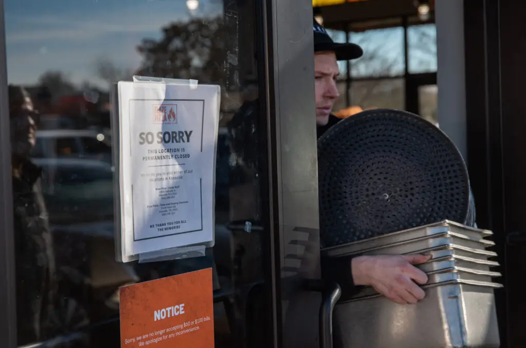 Man carries pizza pots and pans through front door of Blaze Pizza restaurant.