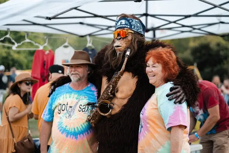 Giant sasquatch character poses with man and woman during festival