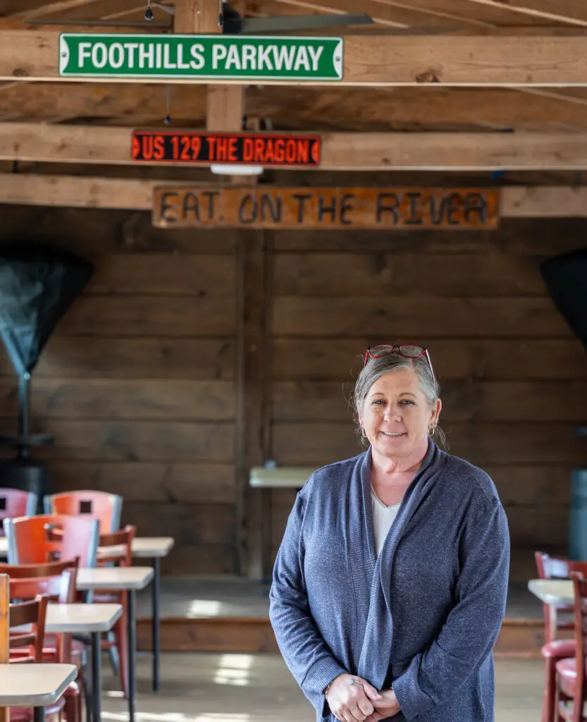 Woman standing in restaurant dining room with Foothills Parkway and US 129 the Dragon signs in the background