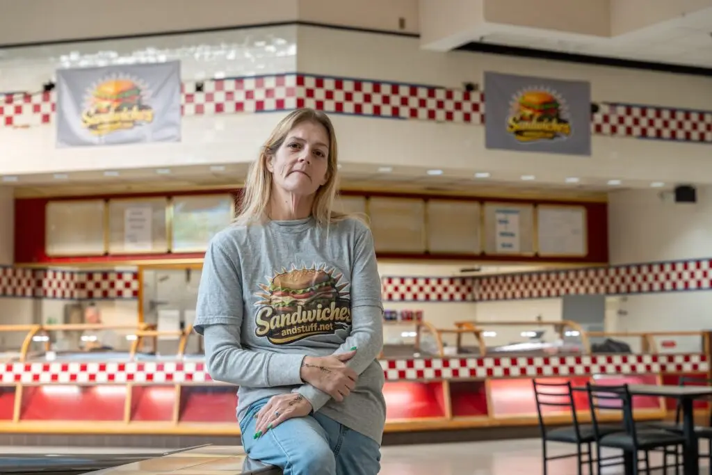 woman wearing a Sandwiches and Stuff t-shirt sits in front of her restaurant
